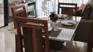 Ruokailutila, jossa on pöytä, tuoleja, riippuvalaisin, seinälle asennettu televisio ja ikkuna, jossa on verhot.