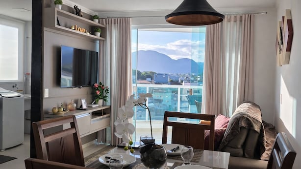 Moderni hotellihuone, jossa on parveke, ruokailutila ja seinälle asennettu televisio.