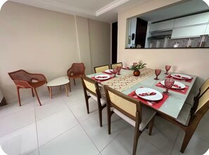 A dining area with a table set for four, surrounded by chairs, and a kitchen area visible in the background.