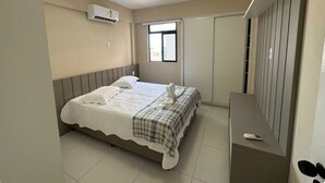 A bedroom with a bed, a bedside table, a window, and an air conditioning unit. - Recanto Nascer do Sol - your refuge in Cabedelo (Cabedelo)