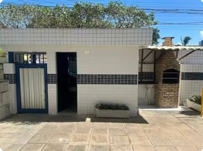 A building with a tiled exterior, a door, a small garden area, and a brick oven structure.