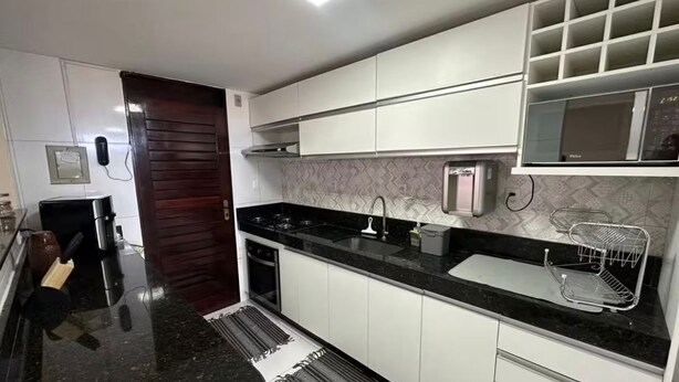 A modern kitchen with white cabinets, a black countertop, a built-in microwave, and a stainless steel sink. - Recanto Nascer do Sol - your refuge in Cabedelo (Cabedelo)