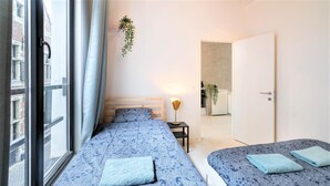 A bedroom with two beds, a window with curtains, a bedside lamp, and a door leading to another room. - Antwerp Central Residence1bbknswifi (Antwerp)