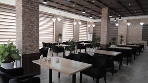 Un restaurante espacioso con paredes de ladrillo, varias mesas, sillas negras y lámparas colgantes.