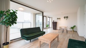 Un salon moderne avec un canapé vert, une table basse en bois et un coin repas comprenant une petite table et des chaises.