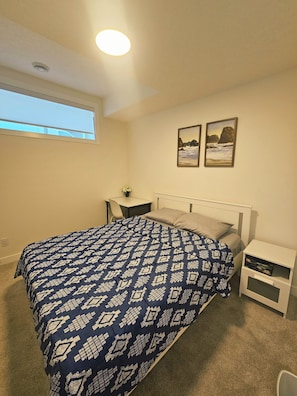 Ein Schlafzimmer mit einem Bett, Nachttischen, einem Fenster und zwei gerahmten Bildern an der Wand.