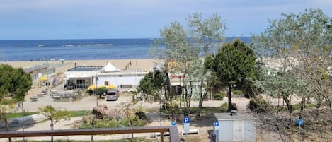 Udsigt over stranden med parkeringsplads, strandparasoller og en bygning med skilt.