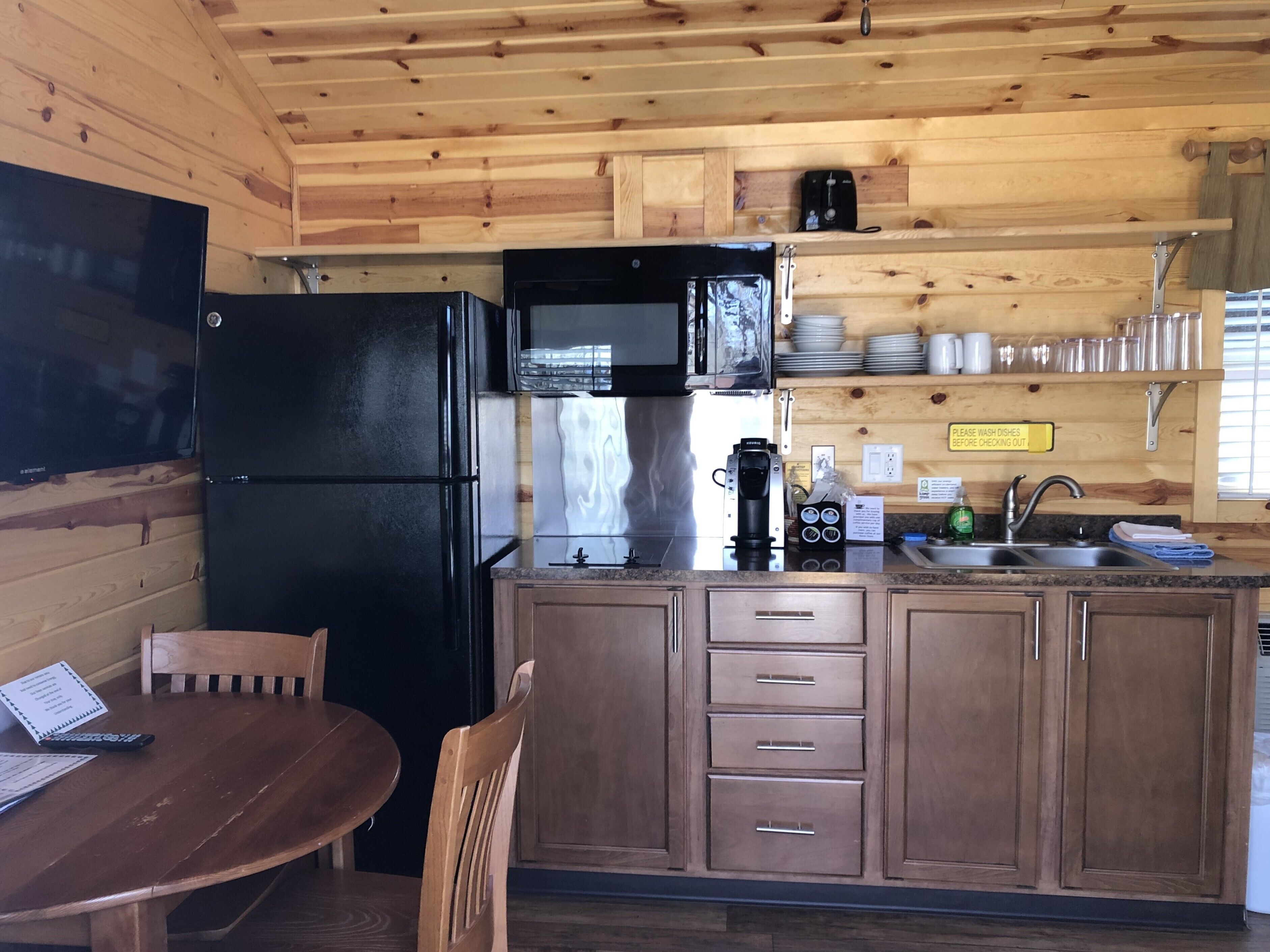 A compact kitchen with wooden cabinets, a black refrigerator, a microwave, and a coffee maker.