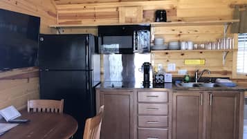 A compact kitchen with wooden cabinets, a black refrigerator, a microwave, and a coffee maker.