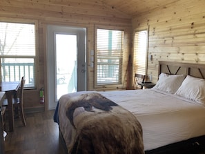 A wooden cabin room with a bed, a table, and a chair.
