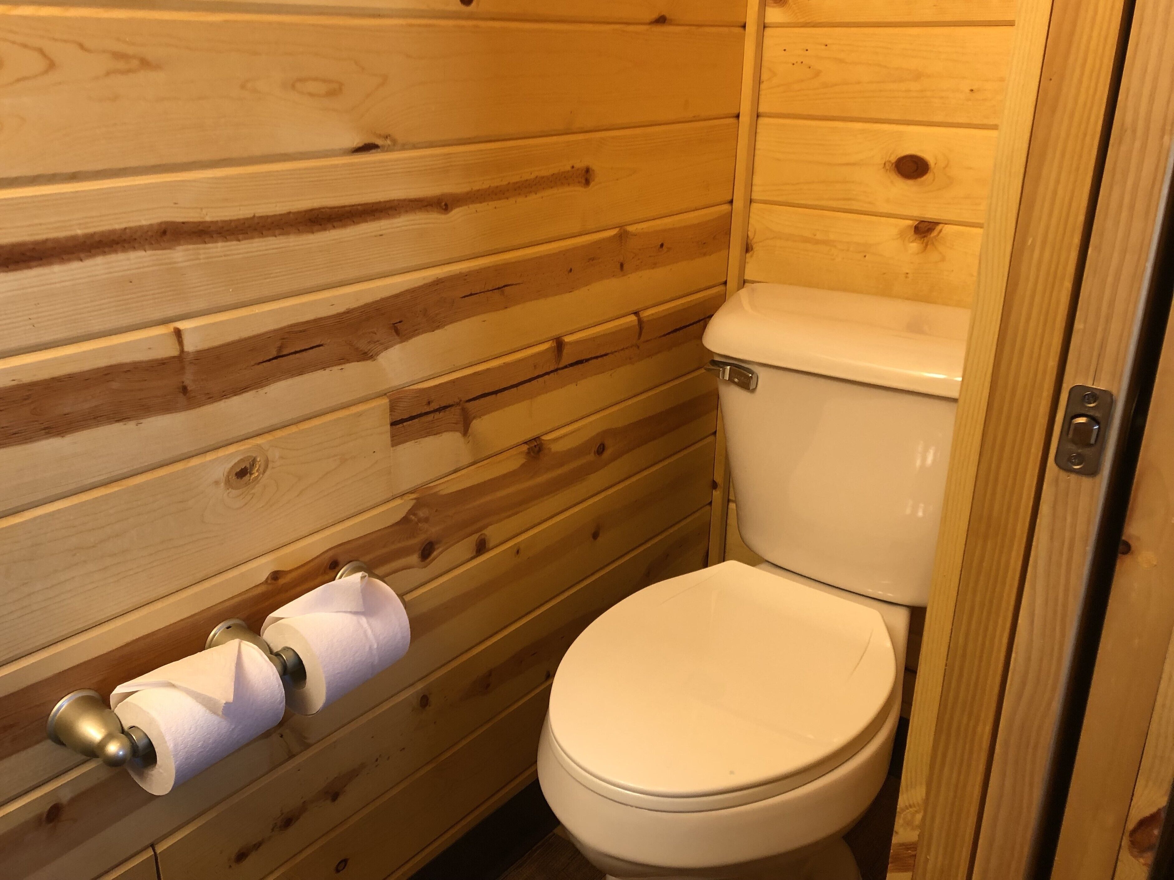 Un baño con paneles de madera, un inodoro y un dispensador de papel higiénico.