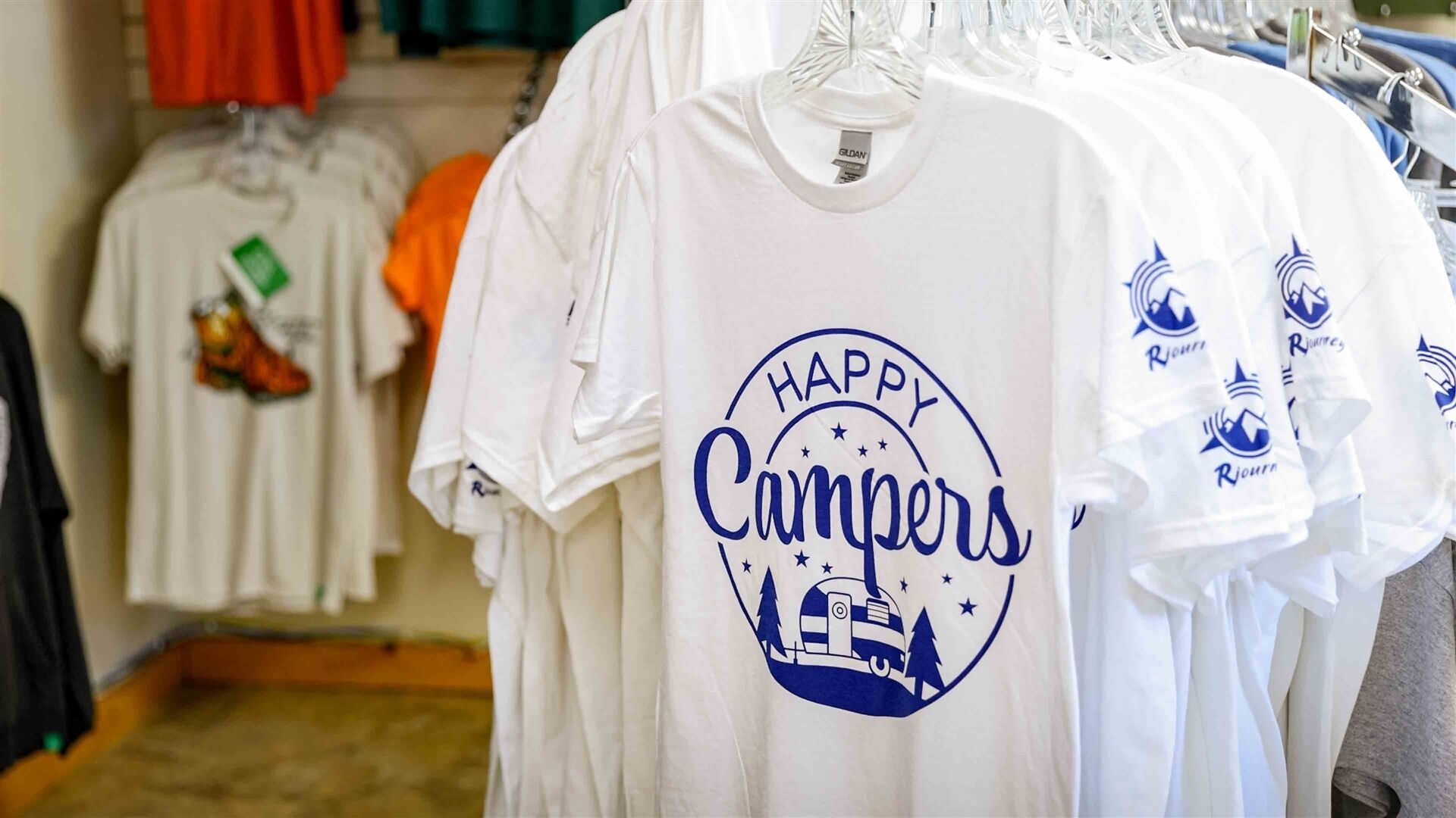 Une pile de t-shirts blancs sur laquelle est imprimé le texte « Happy Campers ».