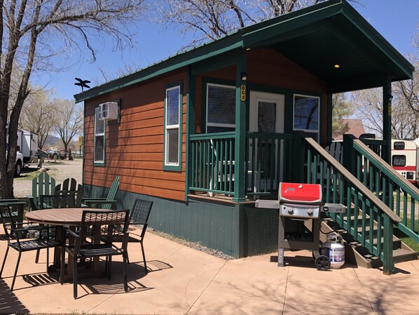 A small cabin with a porch, a table with chairs, and a grill.