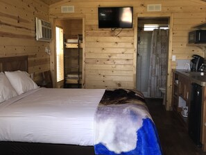 A wooden cabin room with a bed, a television mounted on the wall, and a kitchenette area.