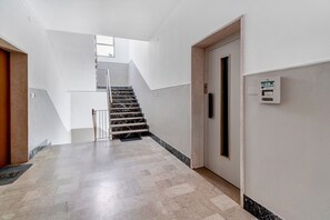 Un interno moderno con una scalinata in marmo, una porta con pannello di controllo e una parete di colore chiaro.