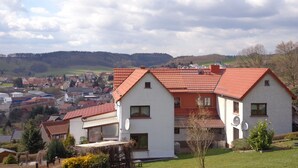 Ein weißes Gebäude mit rotem Dach, Satellitenschüsseln und Blick auf eine Stadt im Hintergrund.