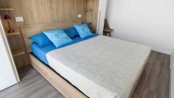 Un lit avec une tête de lit en bois, une literie bleue et une couvre-lit blanche à motifs.