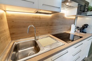 Eine moderne Küche mit Spüle aus Edelstahl, einem schwarzen Induktionskochfeld und Holzschränken.