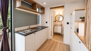 A modern kitchen with a built-in sink, wooden shelves, and a view of the bathroom through an open doorway. - Alya Hill Bodrum (Bodrum)