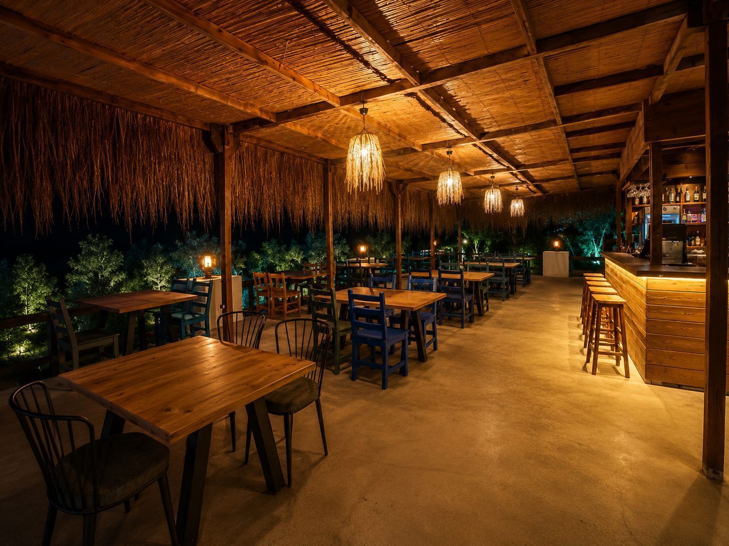 An indoor restaurant with wooden tables and chairs, hanging lights, and a bar area.