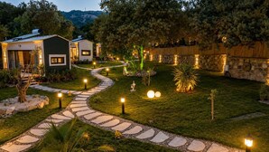 A well-lit garden pathway leading to a modern house with a stone wall and a view of a hill. - Alya Hill Bodrum (Bodrum)
