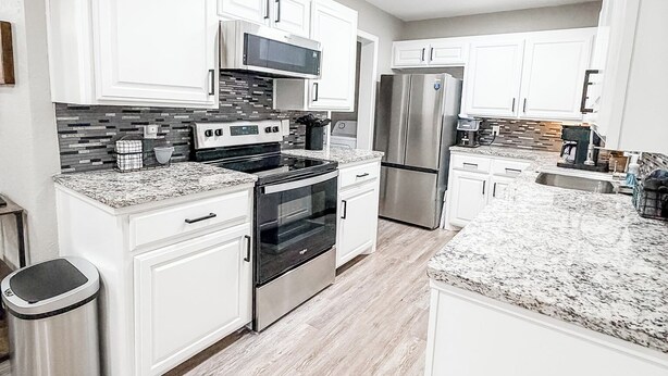 A modern kitchen with white cabinetry, stainless steel appliances, and a granite countertop.