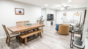 A modern living room with a wooden dining table, a sofa, a TV, and a ceiling fan.