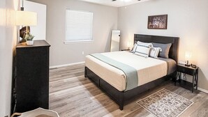 A bedroom with a bed, a ceiling fan, a nightstand, a lamp, a window, and a chair.
