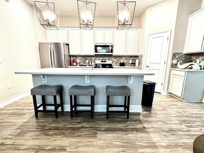 A kitchen with a central island, bar stools, a refrigerator, and a microwave. - Welcoming clean 3-bedroom house in cozy neighborhood in Oakland FL (Winter Garden)