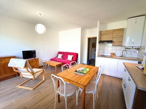 Ein kompakter Wohnbereich mit Esstisch, Stühlen, einem roten Sofa, einem Fernseher und einer Küchenzeile.