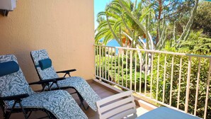 Een balkon met twee loungestoelen, een witte reling en uitzicht op cactussen en palmbomen.