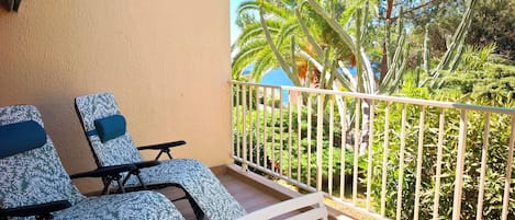 A balcony with two lounge chairs, a white railing, and a view of cacti and palm trees.