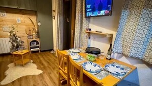 Ein Essbereich mit einem Holztisch, gedeckt für zwei Personen, einem an der Wand montierten Fernseher und einem gemusterten Vorhang.