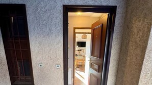 Ein Flur, der zu einem Raum mit einer Tür, einem kleinen Fenster und einer Fußmatte führt.