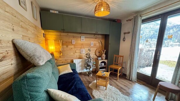 Ein gemütliches Wohnzimmer mit einem grünen Sofa, Holzwänden, einem kleinen Tisch und einem Weihnachtsbaum.