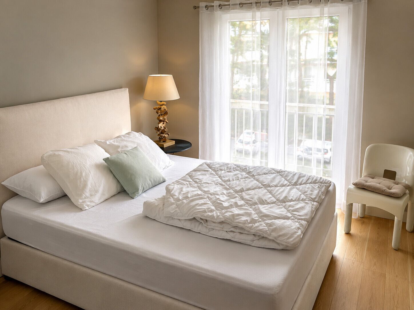 Un lit bien fait, avec des oreillers, une lampe de chevet et une chaise.