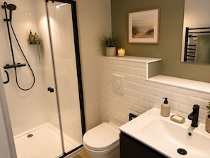 A modern bathroom with a glass-enclosed shower, a toilet, a sink with a mirror, and a shelf with toiletries and a candle. - Beautiful apartment with balcon in La Baule (La Baule-Escoublac)