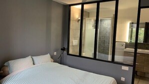 Un dormitorio con una cama, una mesita de noche, una lámpara y una puerta corrediza de vidrio que da a un baño.