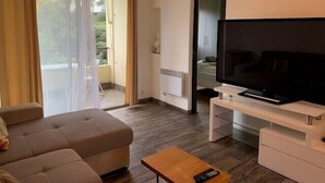 Una sala de estar moderna con un sofá, una mesa de centro, un televisor sobre un mueble bajo y un ventanal corredero que da a un espacio exterior.
