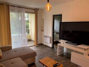 A modern living room with a sofa, a coffee table, a TV on a stand, and a sliding glass door leading to an outdoor area. - Beautiful 45 m² apartment with balcony in Nice (Nice)