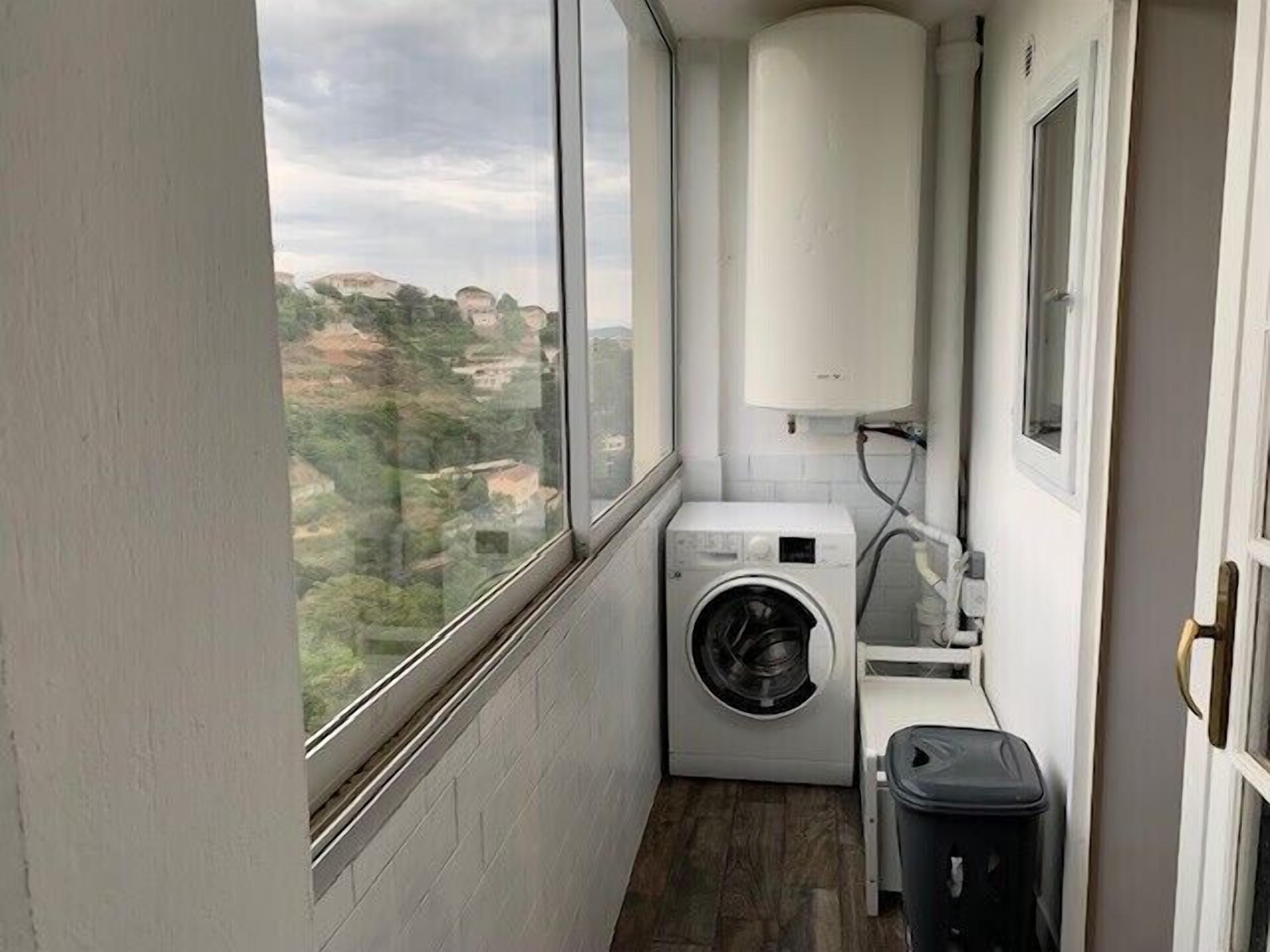A compact laundry room with a washing machine, a small sink, and a trash bin.