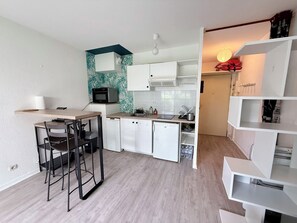 Una cucina compatta con mobili bianchi, un forno a microonde, un lavello e un'area pranzo con sedie.