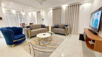 Ein modernes Wohnzimmer mit Sofa, Sessel, Couchtisch und Fernseher.
