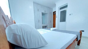 Un lit bien fait, avec du linge de lit blanc, dans une pièce aux murs blancs et dotée d’une tête de lit en bois.