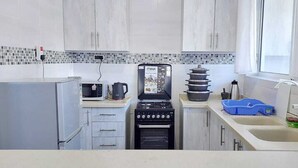 Une cuisine compacte équipée d’un four à micro-ondes, d’une cuisinière et d’un évier, avec un dosseret carrelé et des meubles de couleur claire.