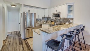A modern kitchen with white cabinets, stainless steel appliances, a granite countertop, and a bar stool area. - Ski In, Modern, Cozy Condo on Aspen Mountain - 1 Block from Gondola & Town (Aspen)
