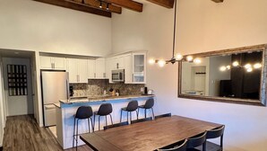 A modern kitchen with white cabinets, a large island with bar stools, and a dining area with a long wooden table and chairs. - Ski In, Modern, Cozy Condo on Aspen Mountain - 1 Block from Gondola & Town (Aspen)