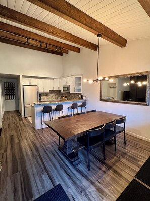 Eine moderne Küche mit weißen Schränken, einer großen Kochinsel mit Barhocker und einem Essbereich mit langem Holztisch und Stühlen.