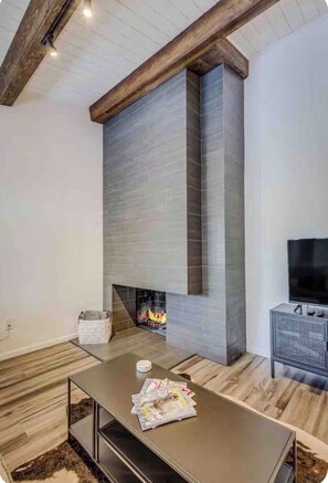 Ein modernes Wohnzimmer mit Kamin, Holzbalken und einem Fernseher auf einem Schrank.