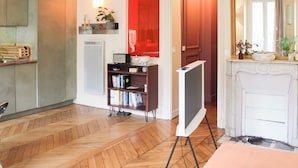 Una habitación con suelo de espiga, un televisor sobre un mueble, una estantería y un espejo.